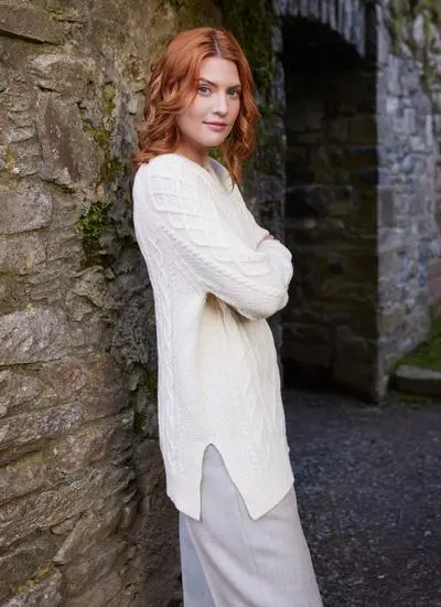 Side shot of red haired woman in abbey wearing white Aran sweater with both arms folded
